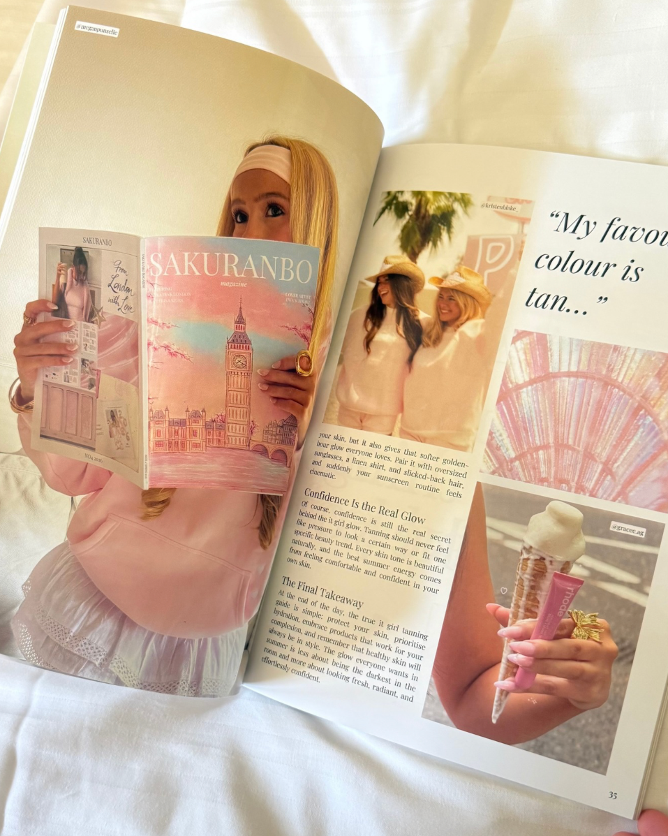 An open magazine spread laid on white fabric, featuring a pastel pink cover story with a woman holding a book titled 'Sakuranbo' and other inset photos and text on the pages.
