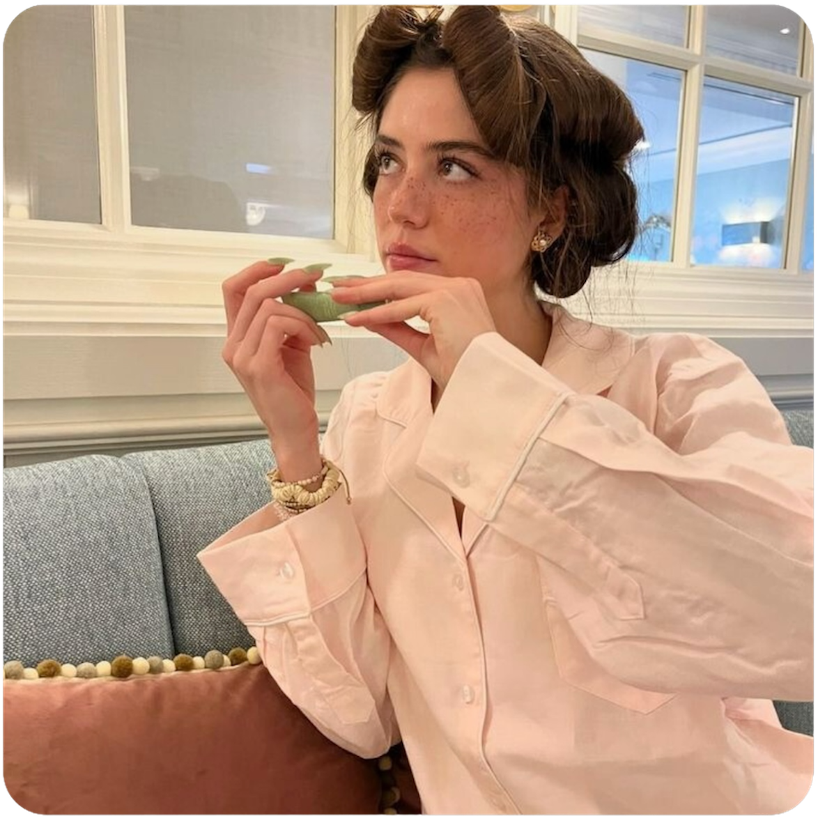 Woman in a light pink shirt sitting on a couch indoors.
