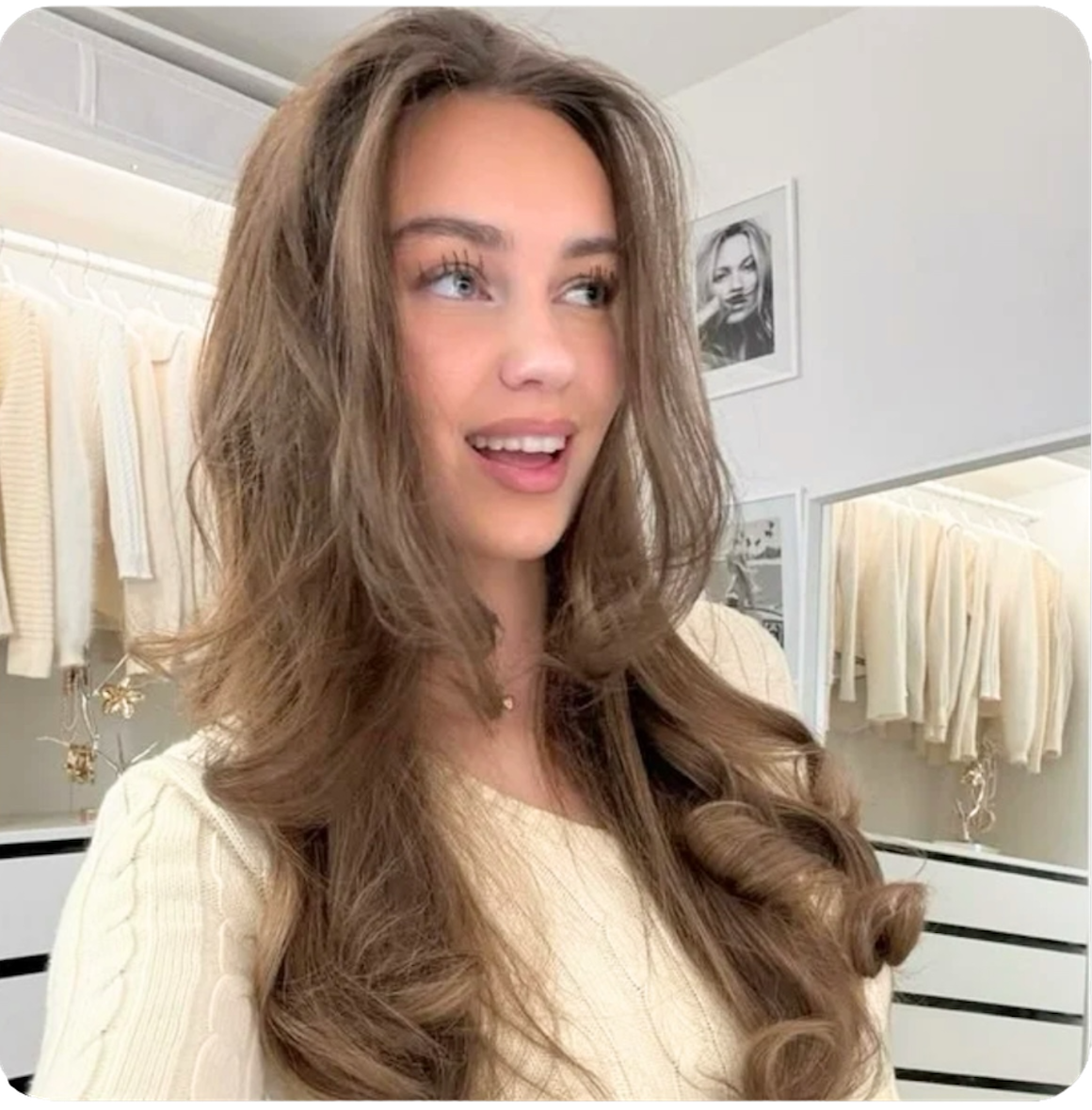 Woman with long, wavy hair in a room with clothing racks.